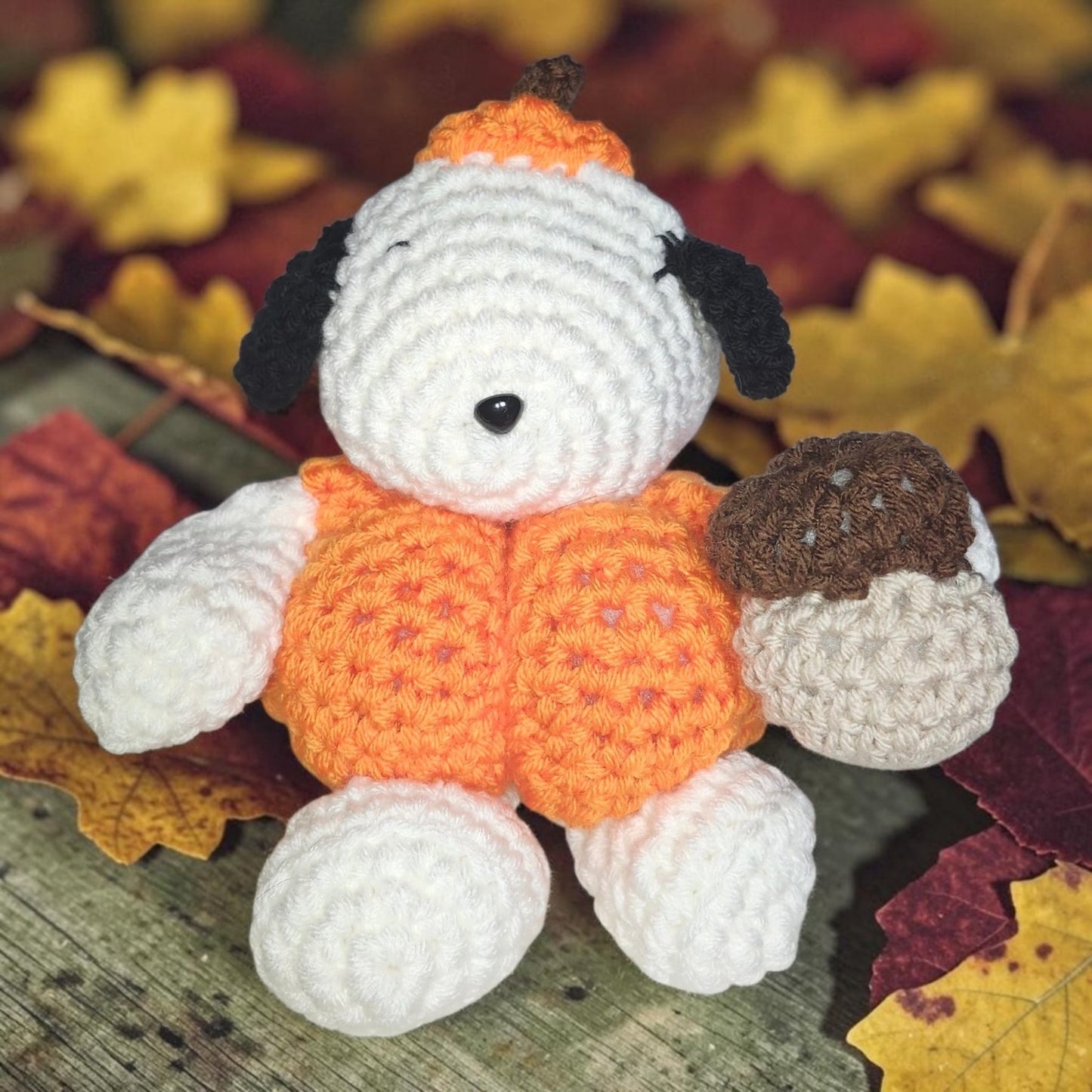 Handmade Snoopy-inspired crochet plushie dressed in a pumpkin costume and holding an acorn.
